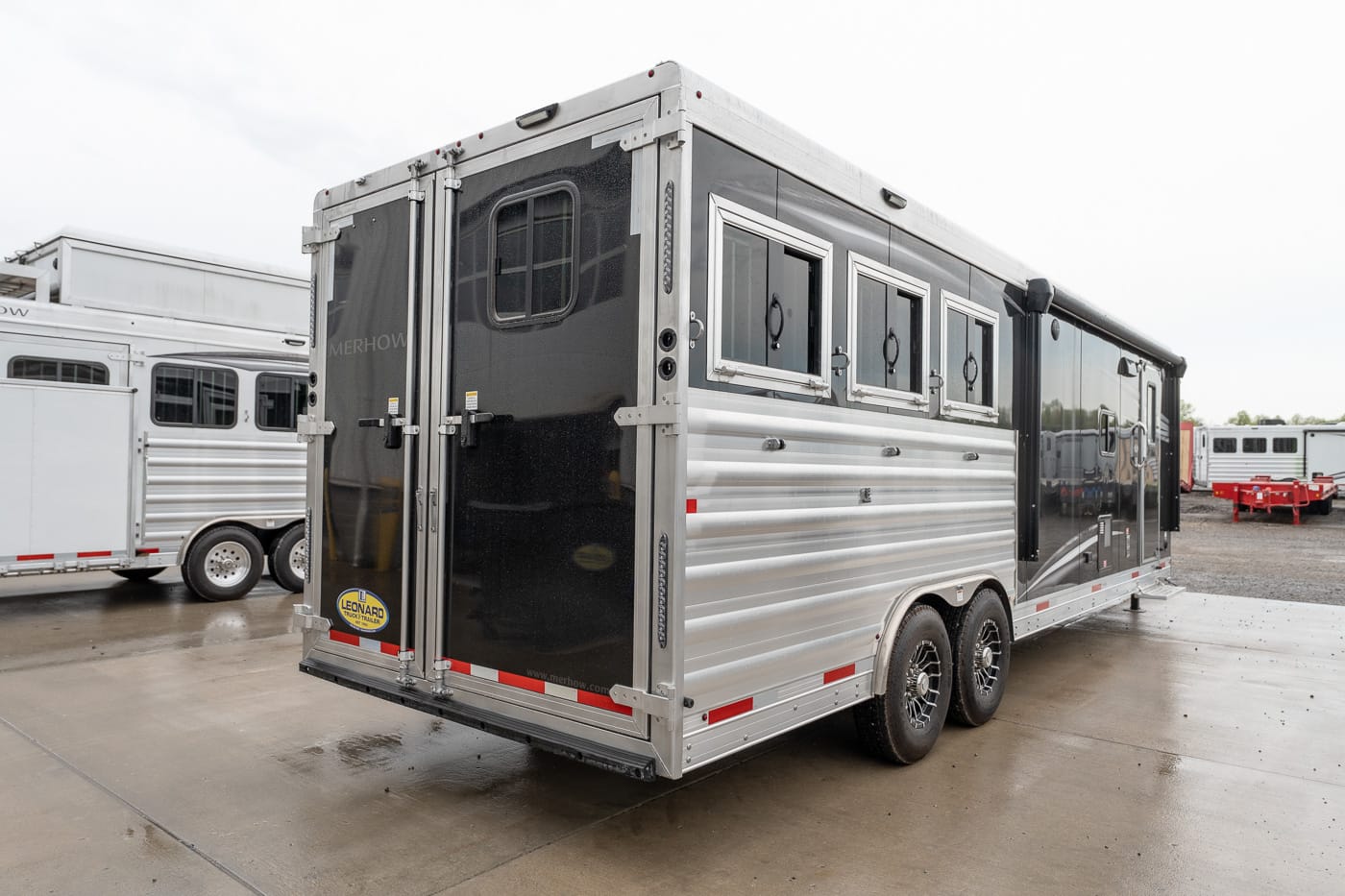 Silver two-axle horse trailer with side windows and rear double doors in a dealership yard? (informative)