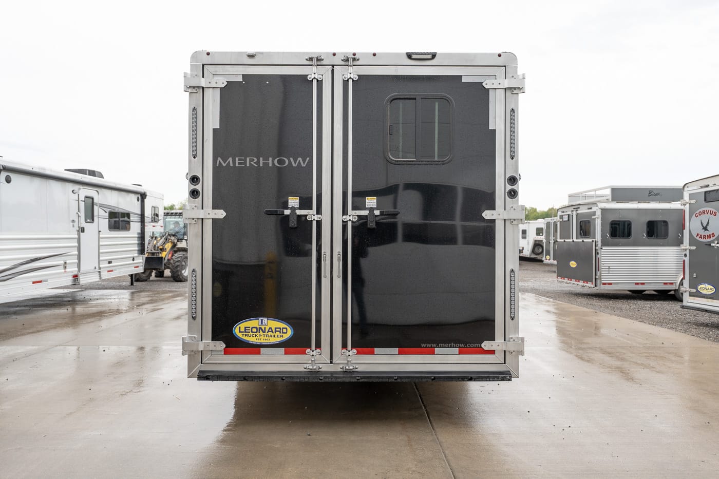 Rear view of a glossy black Merhow horse trailer in a trailer lot with other trailers nearby.