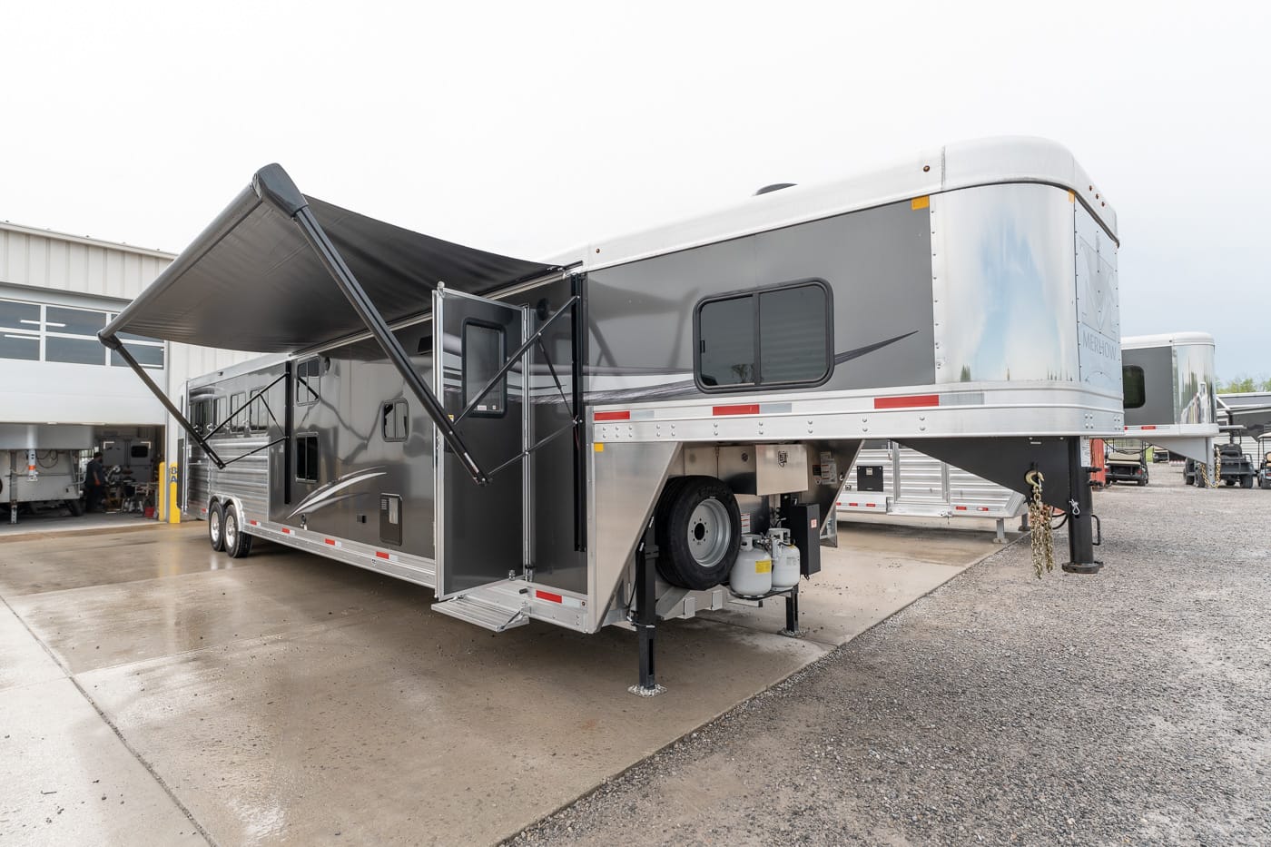A large gray fifth-wheel trailer with an extended awning deployed beside a service area.