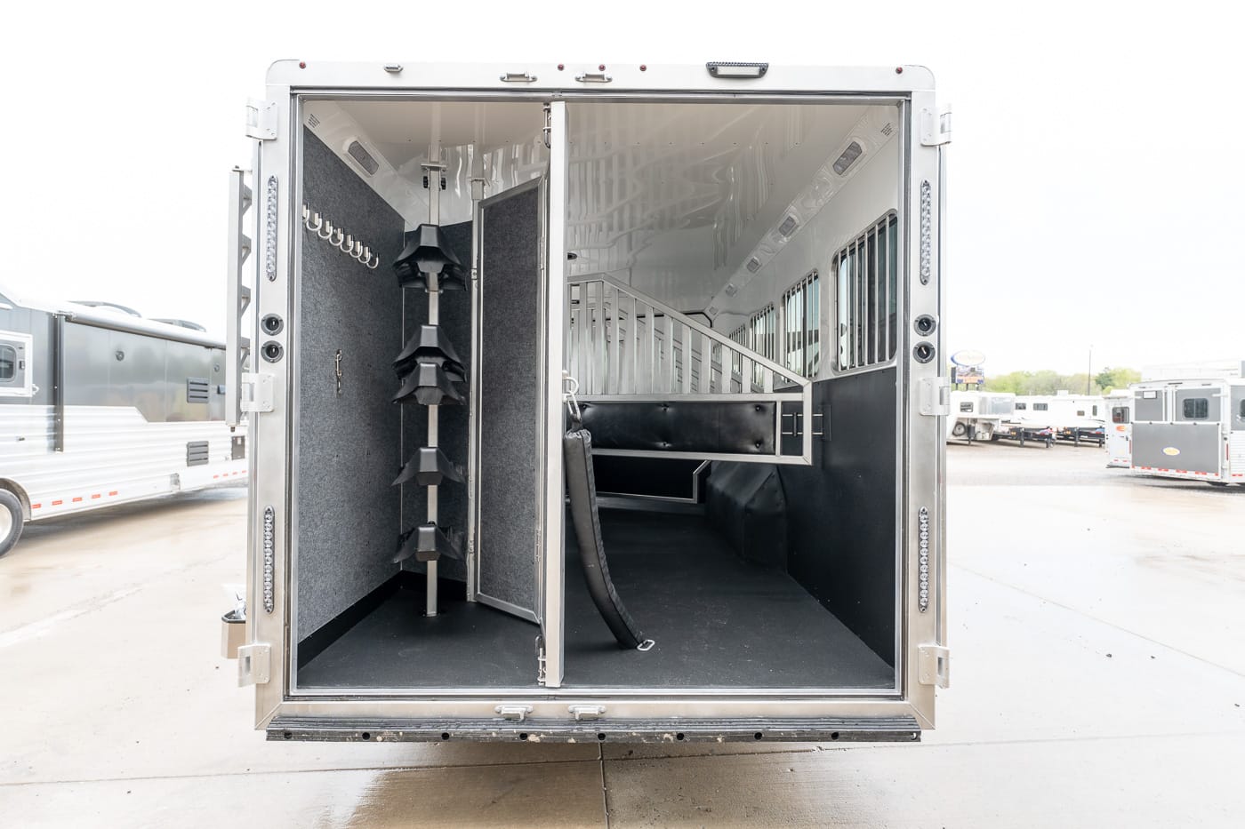 Rear view of a horse trailer interior with a partitioned stall on the right and tall saddle racks on the left for tack storage on a trailer.