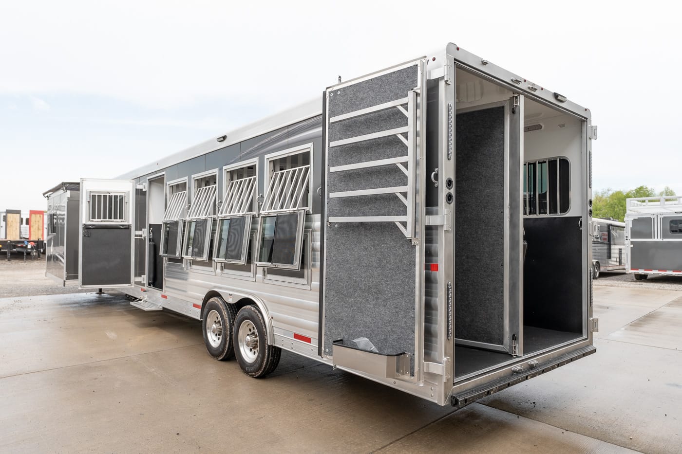 Silver horse trailer with open rear ramp and side windows, showing multiple stalls and ventilation bars.