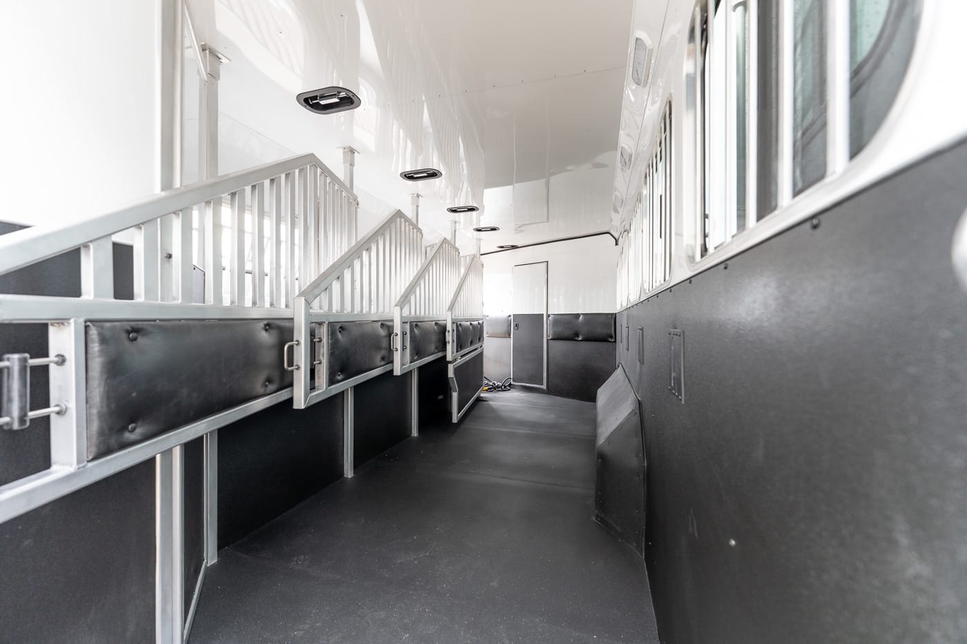 Interior of a horse trailer: white walls, black padded stall walls, and metal dividers along the left edge of the aisle.