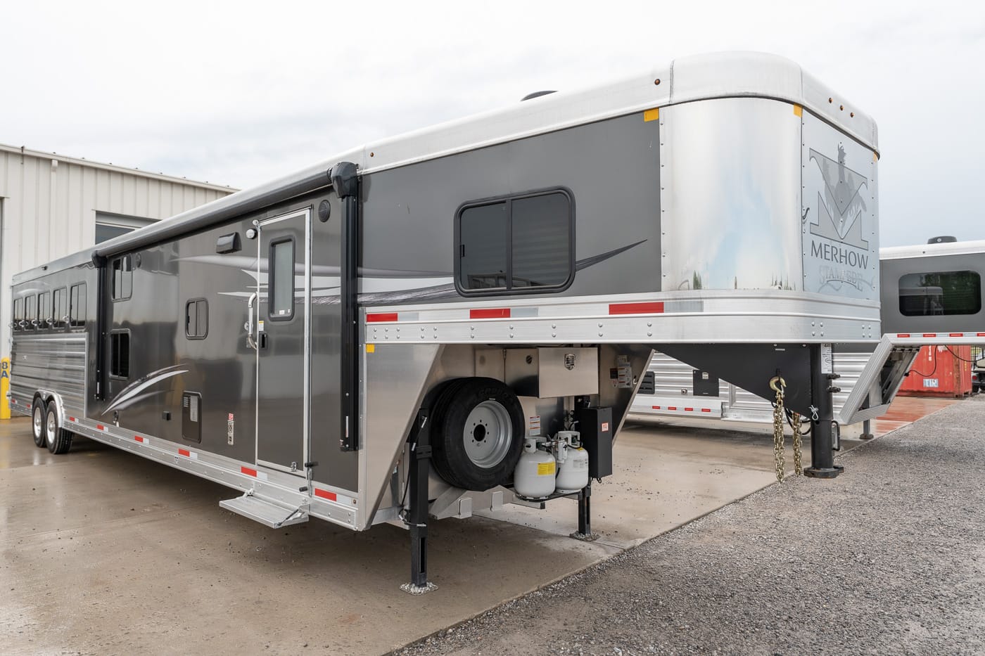 Fifth‑wheel travel trailer parked on a concrete lot, stabilizing jacks down and propane tanks visible under the hitch area.
