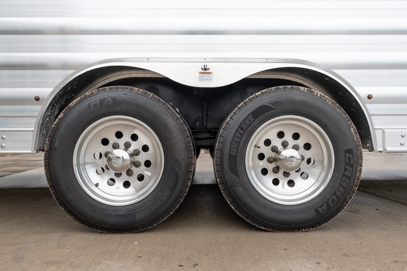 Dual-axle trailer wheels with metal fenders and chrome hubs on a silver trailer side panel2-sided tires.