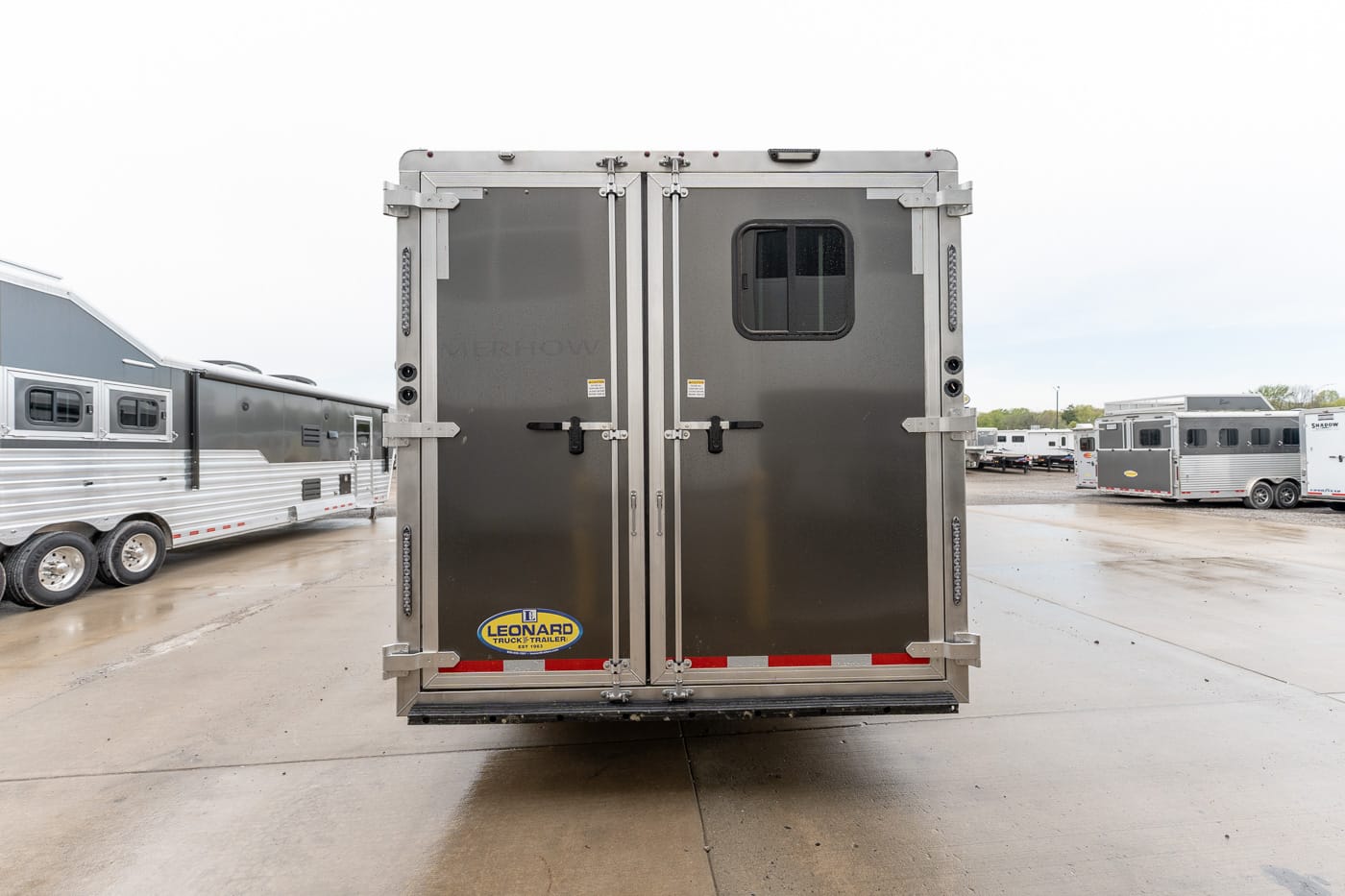 Rear view of a large metal horse trailer with double doors, a small window, and a Leonard logo at the bottom left.
