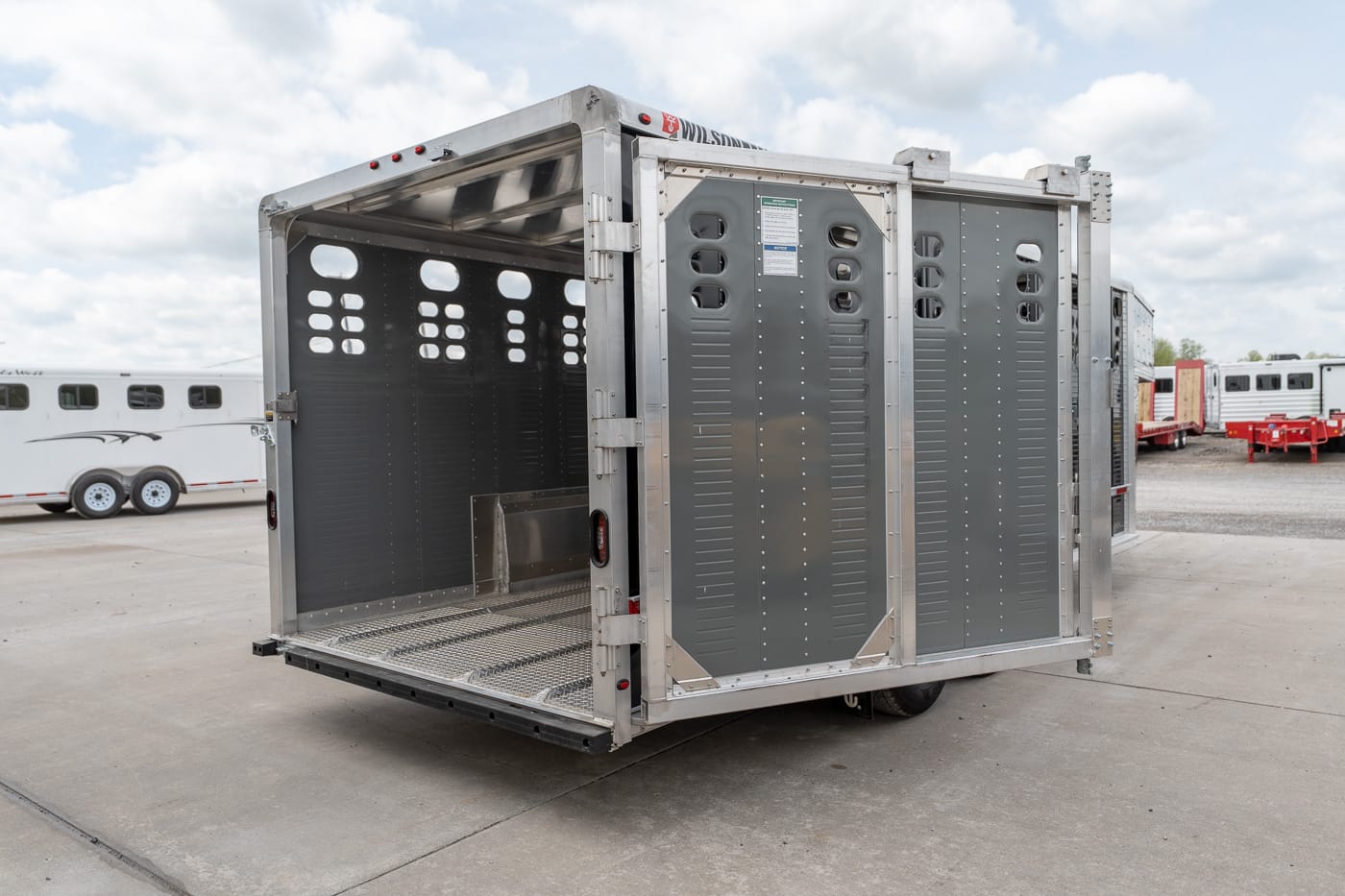 Open aluminum livestock trailer on a concrete lot, with ventilation holes along the walls.