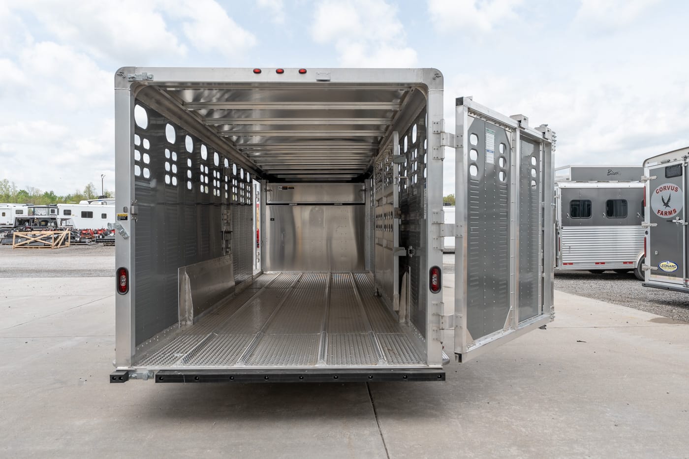 Empty aluminum livestock trailer with open rear doors, showing perforated side walls and metal floor on a sunny day.