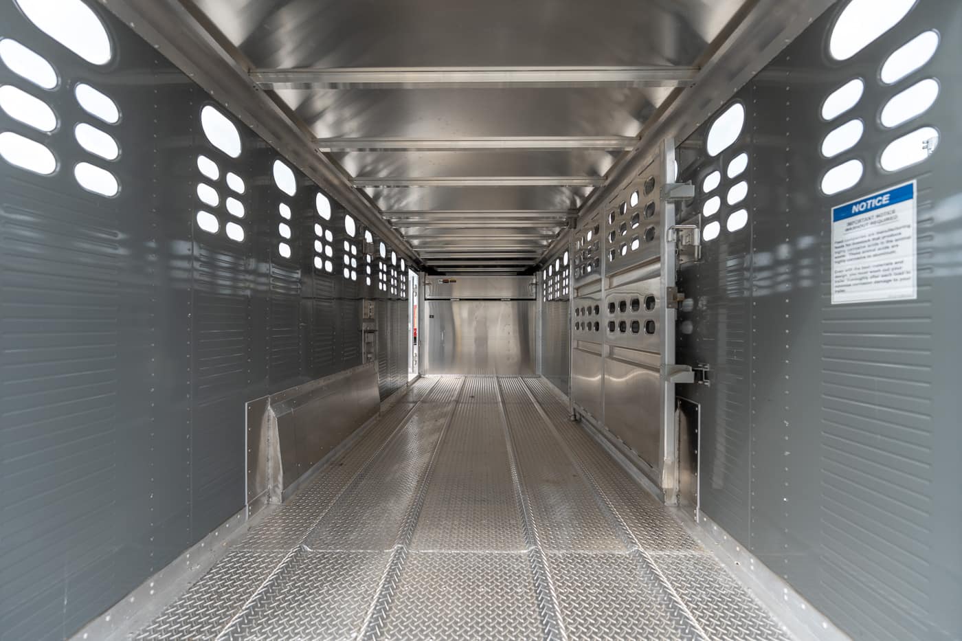 Interior of an empty aluminum livestock trailer with perforated side walls and a diamond-plate floor