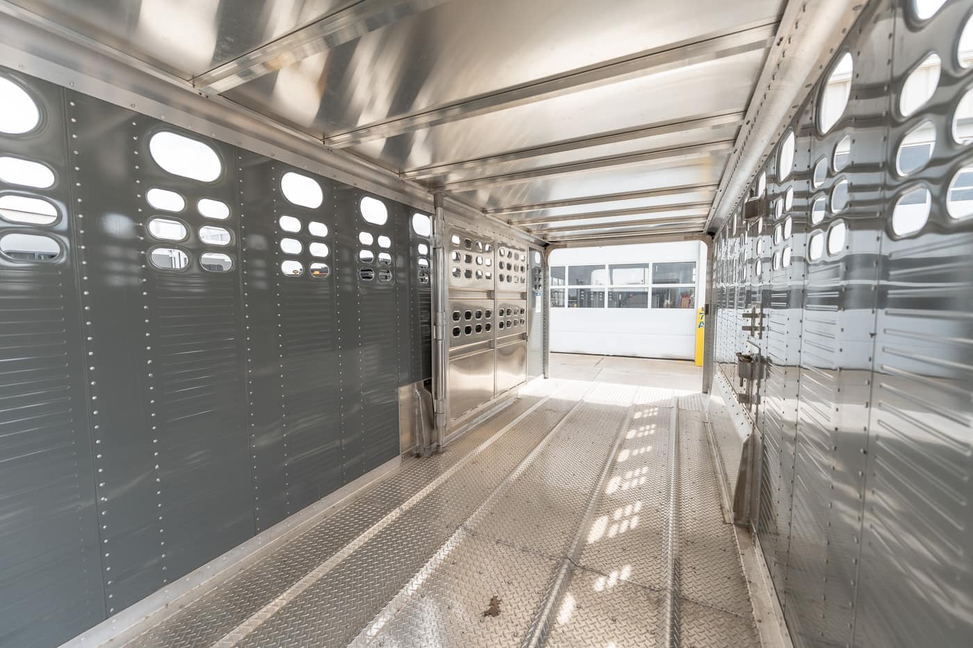 Empty stainless-steel livestock trailer interior with riveted walls and ventilation holes on both sides.