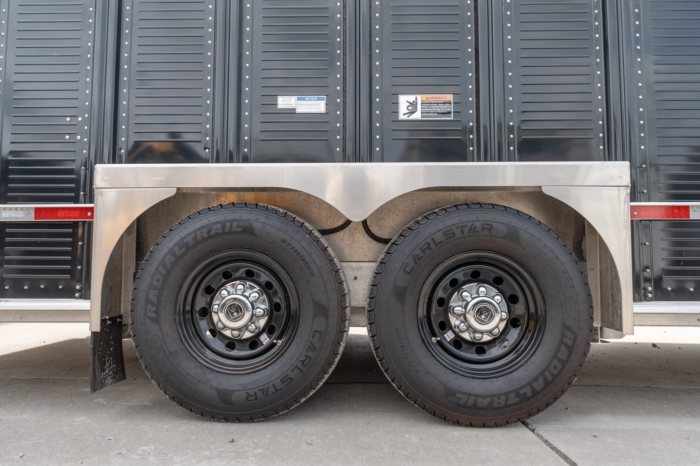 Side view of a dual-axle trailer with two black steel wheels and metal fenders over the tires.