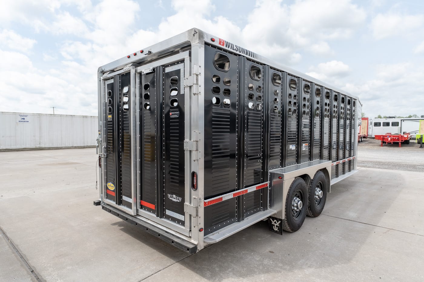 Two-axle livestock trailer with black vented sides on a concrete lot, ready for transport of cattle or other livestock.