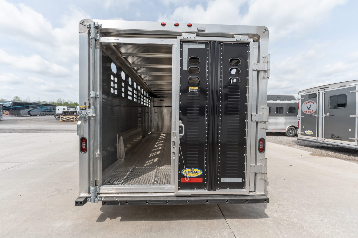 Rear of an open aluminum trailer with a black interior panel and perforated walls, empty floor, and daylight streaming inside.
