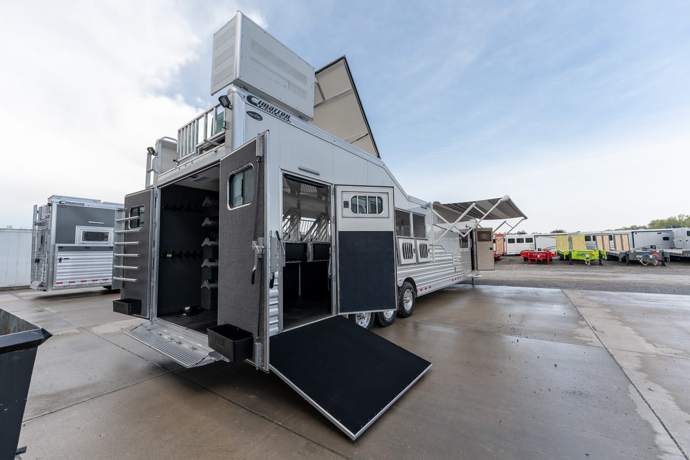 Large silver horse trailer with open rear doors and ramp, exposing interior stalls and tack storage.