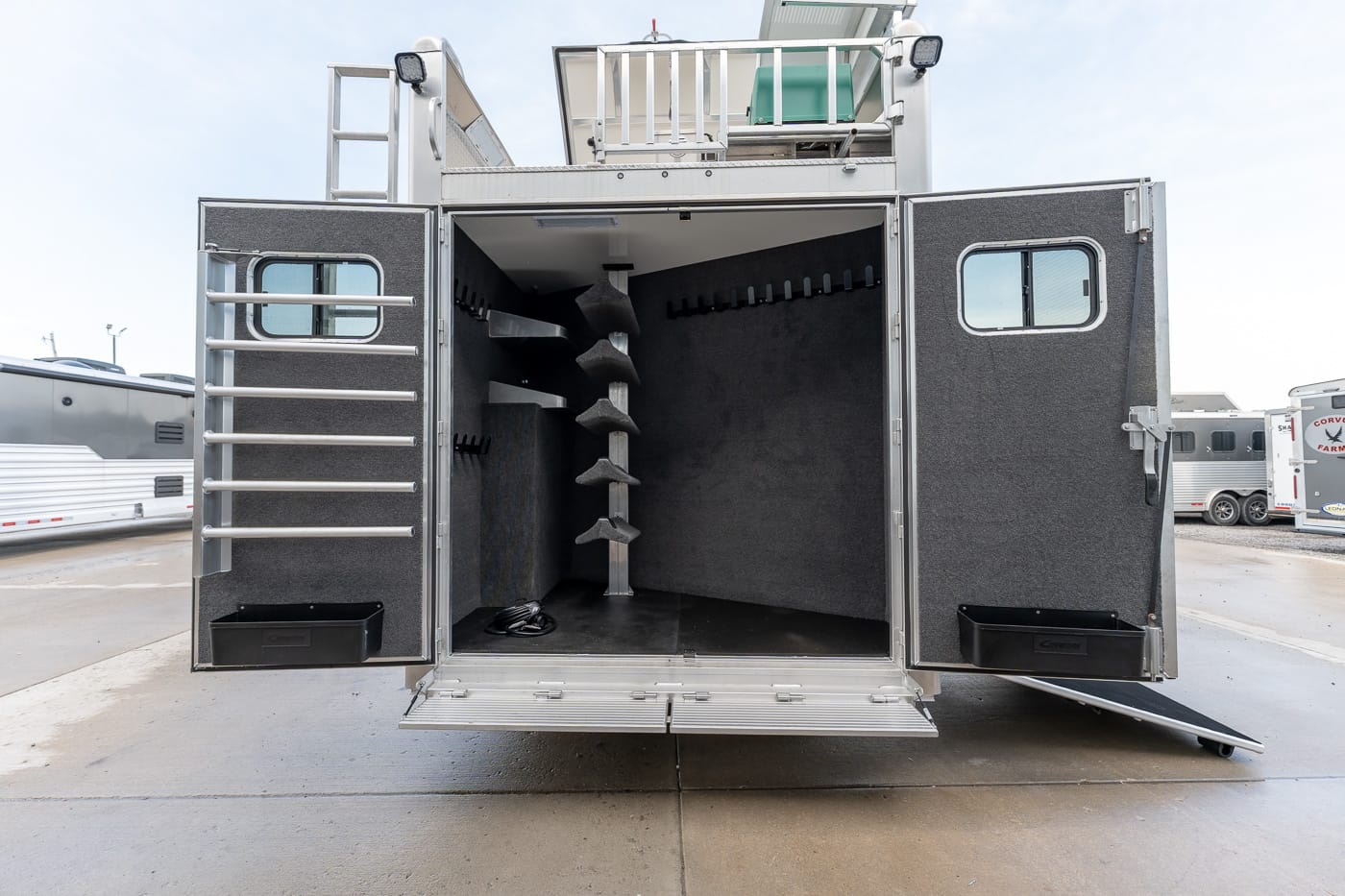 Open rear of a utility trailer with carpeted walls, showing side storage racks and an open ramp for gear loading