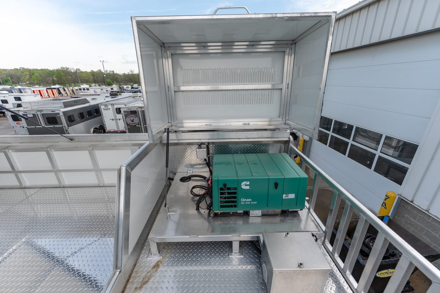 Green Onan generator mounted on a diamond-plate service deck with open hood, in a utility trailer area.