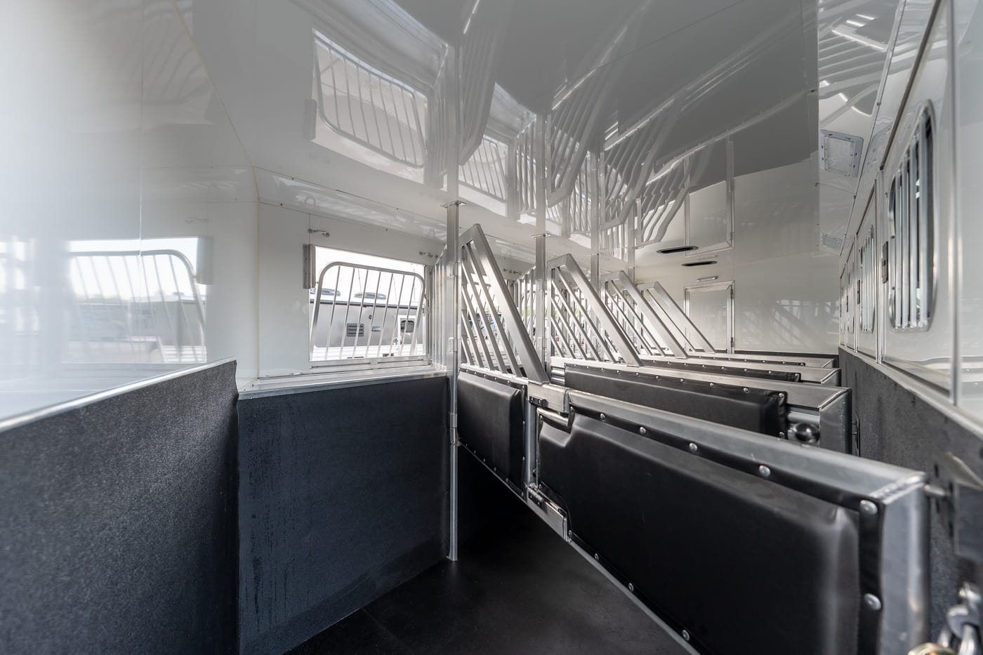 Interior of an empty passenger train car with black cushioned benches along the sides and metal dividers facing an aisle, windows to the left