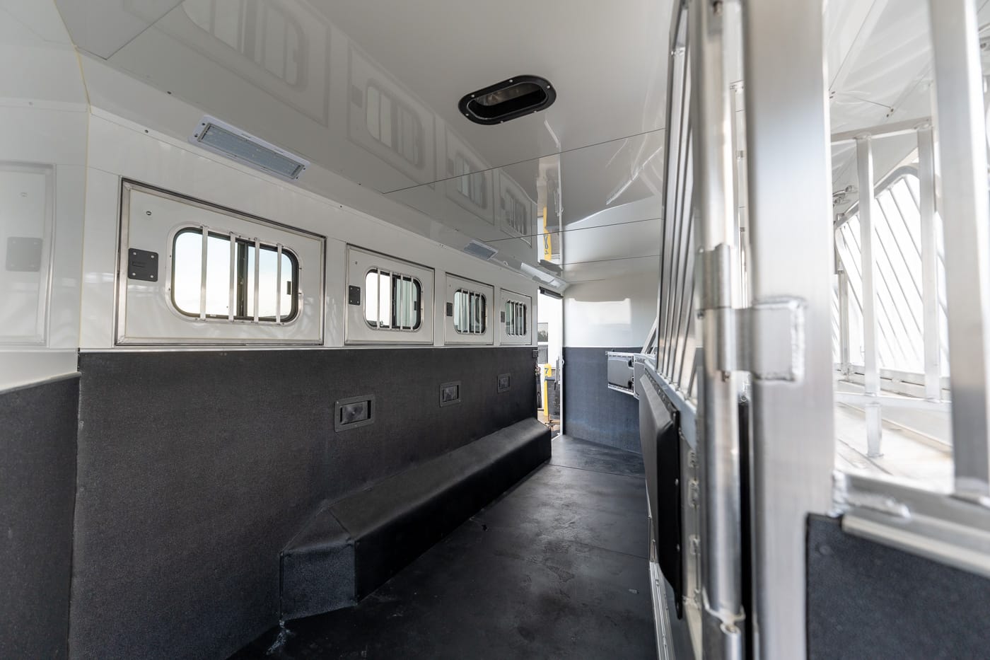 Interior of a white aluminum horse trailer with padded lower walls, small rectangular windows along the stall wall, and a dark non-slip floor.