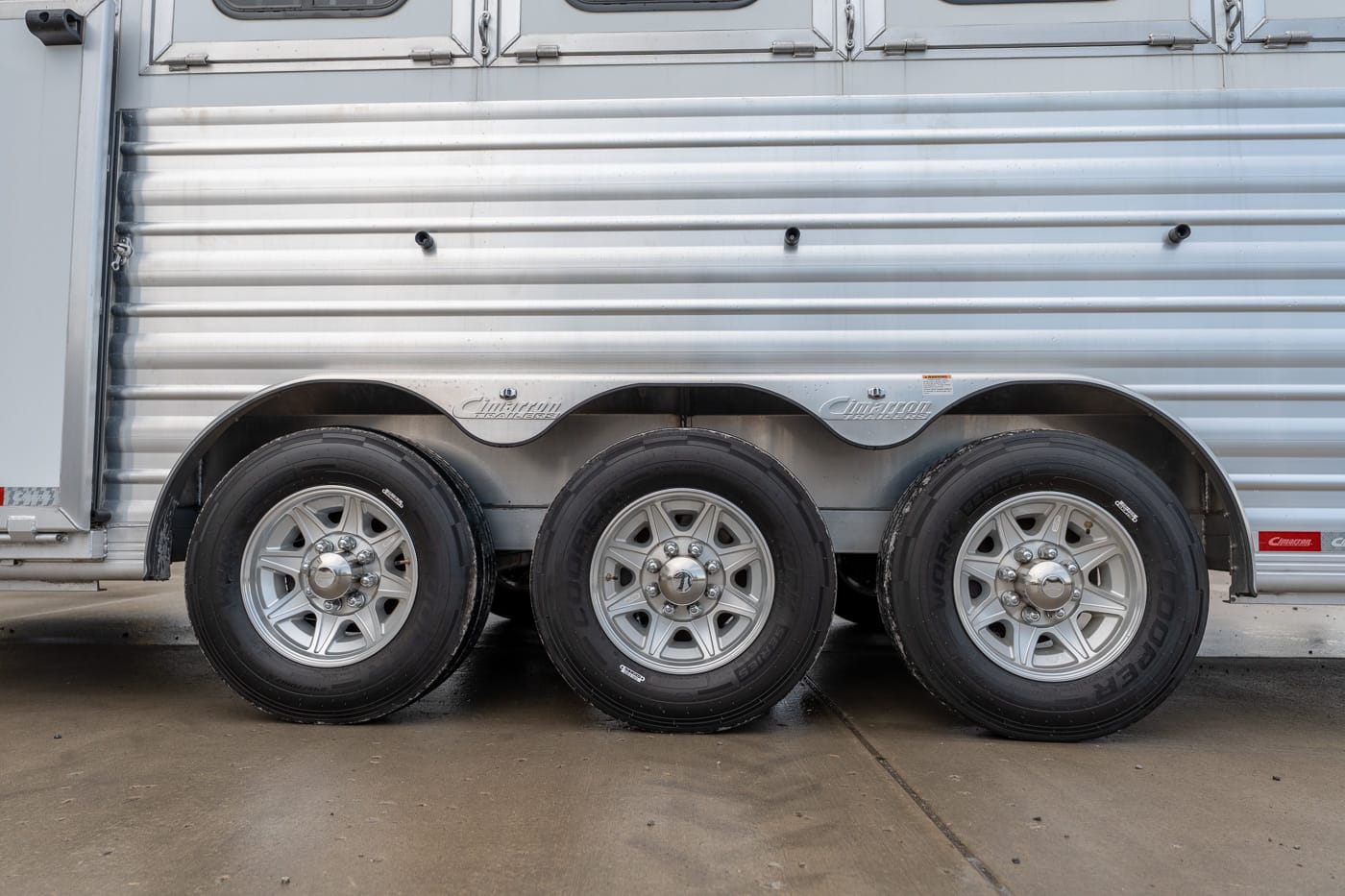 Triple-axle trailer with silver wheels and black tires along a corrugated metal side panel.