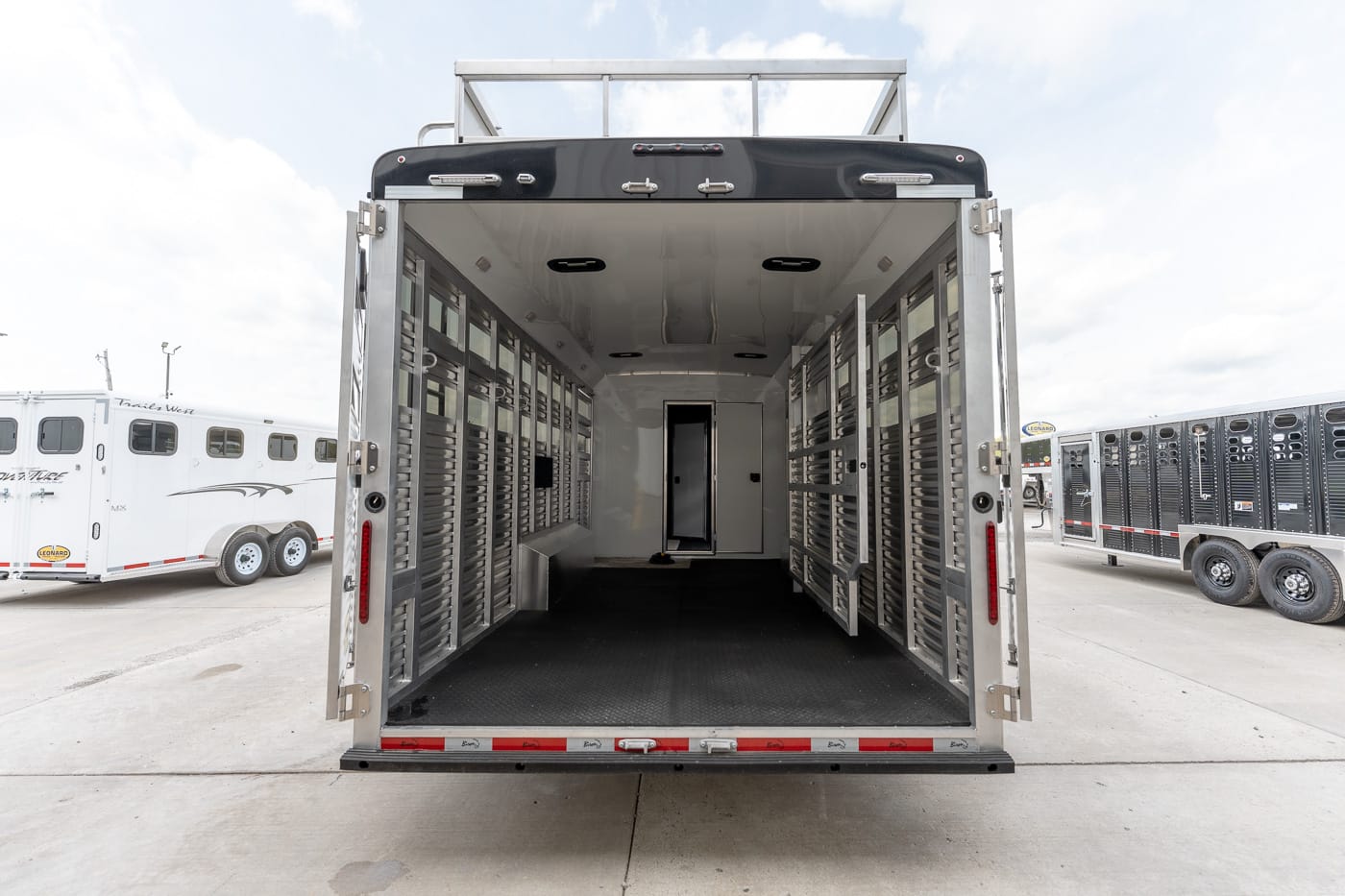 Empty stainless steel horse trailer interior with stalls along both sides and open rear doors