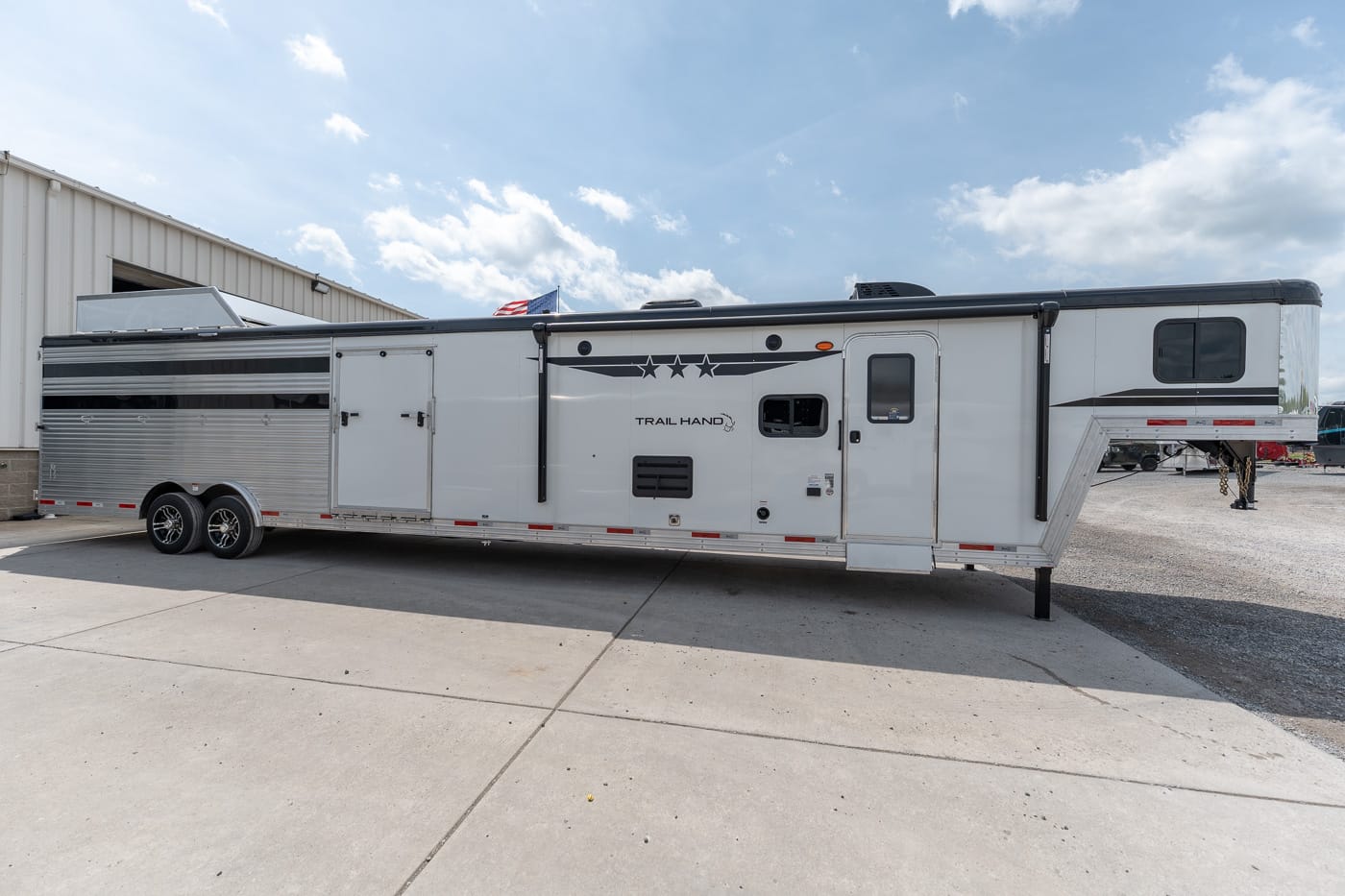 White gooseneck horse trailer parked on concrete with an American flag and 'Trail Hand' branding on the side (long dual-axle trailer).