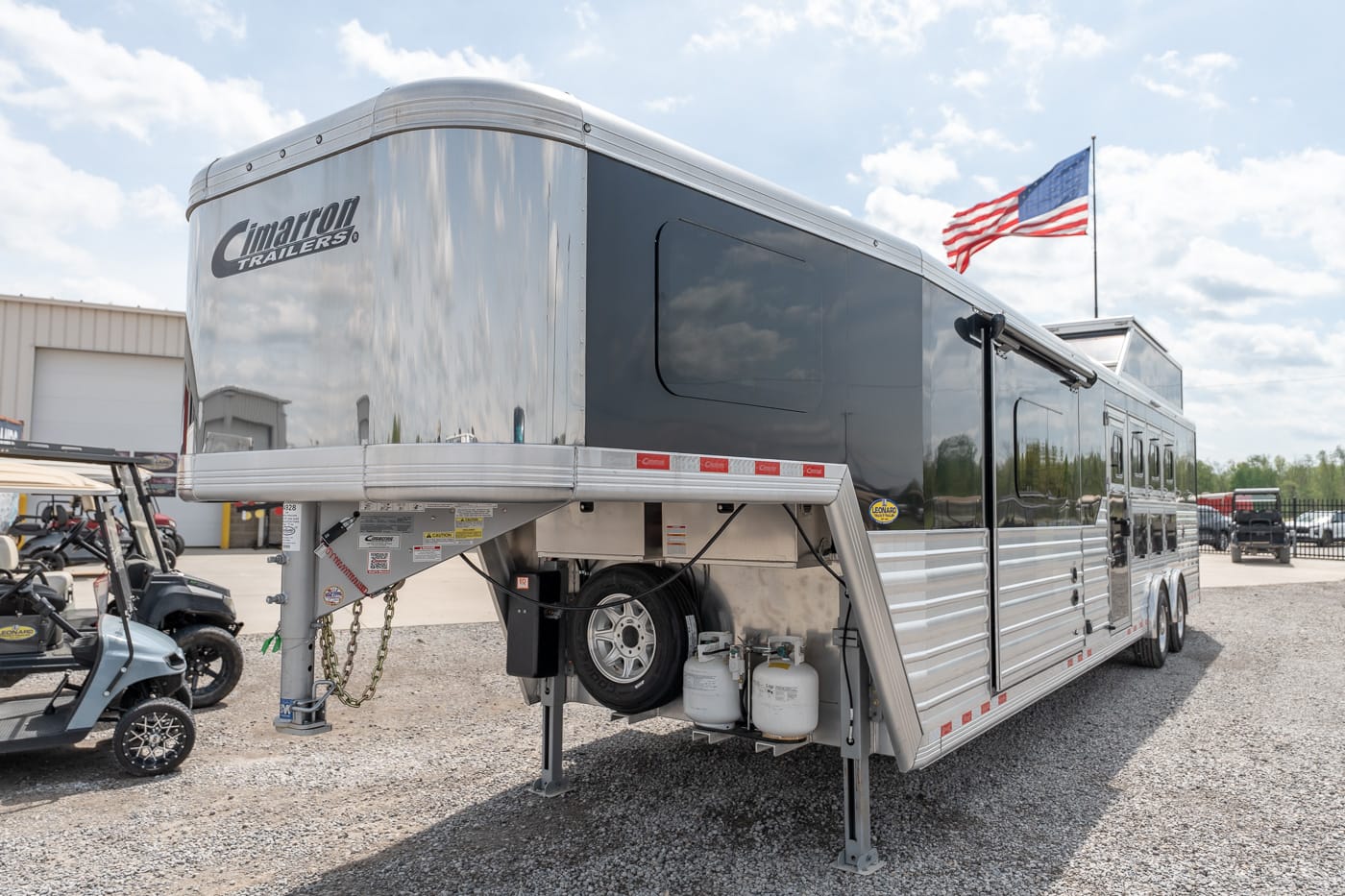Silver Cimarron gooseneck horse trailer on a gravel lot, with spare tire and propane tanks visible in front area.