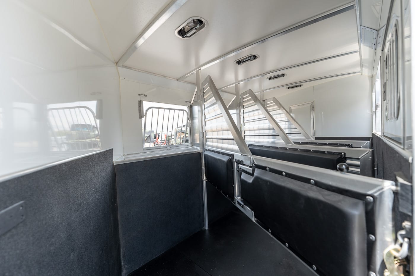 Interior of a metal livestock trailer with partitioned stalls and black padded walls for animals.
