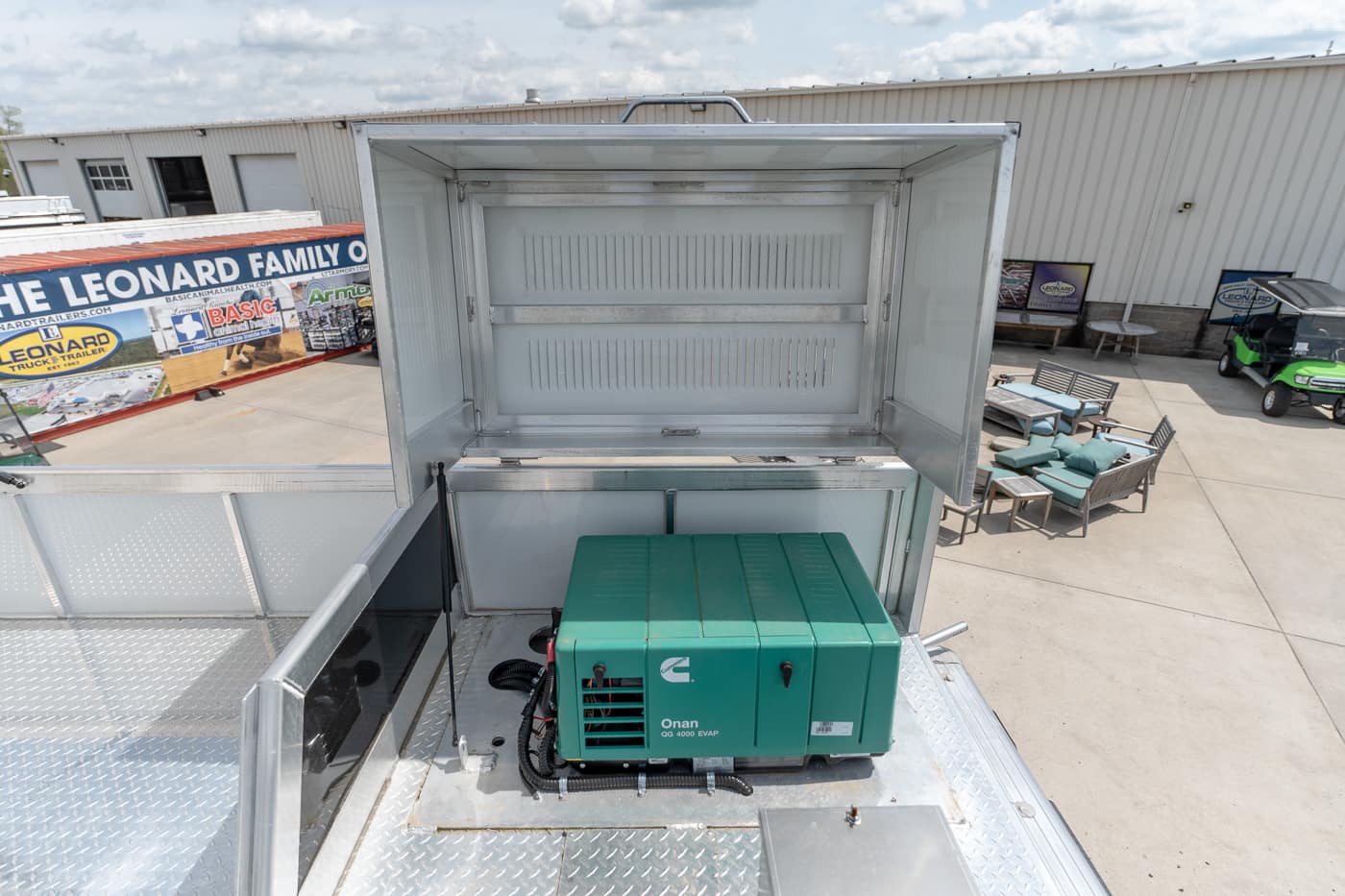 Green Onan generator installed in a metal truck bed with a raised, open storage box above it, outdoor dealership setting nearby.