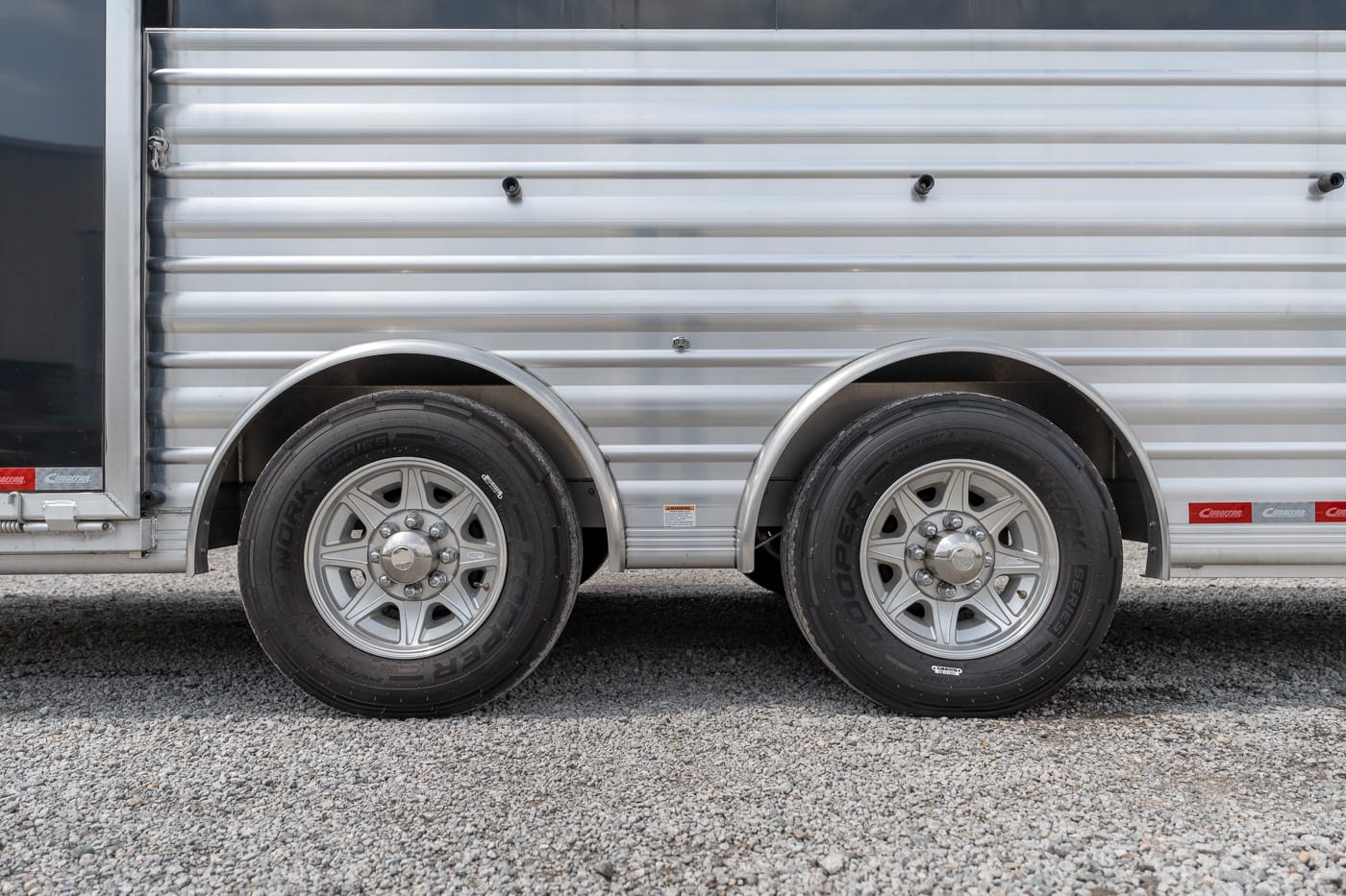 Side view of a silver cargo trailer with two wheels and rounded wheel arches, parked on gravel ground