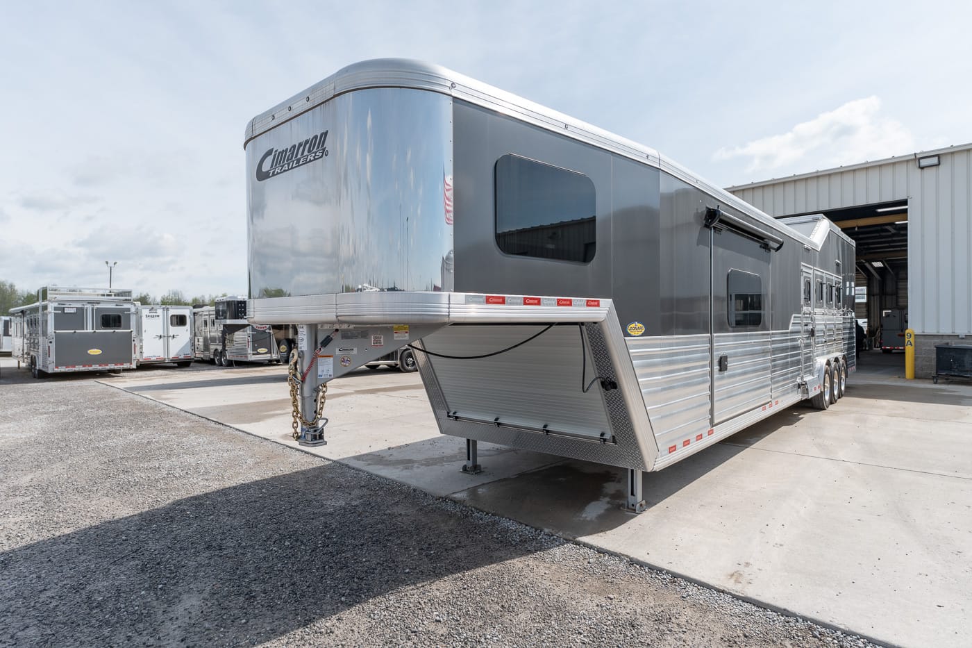 Shiny silver gooseneck horse trailer parked in a dealership lot with other trailers nearby.