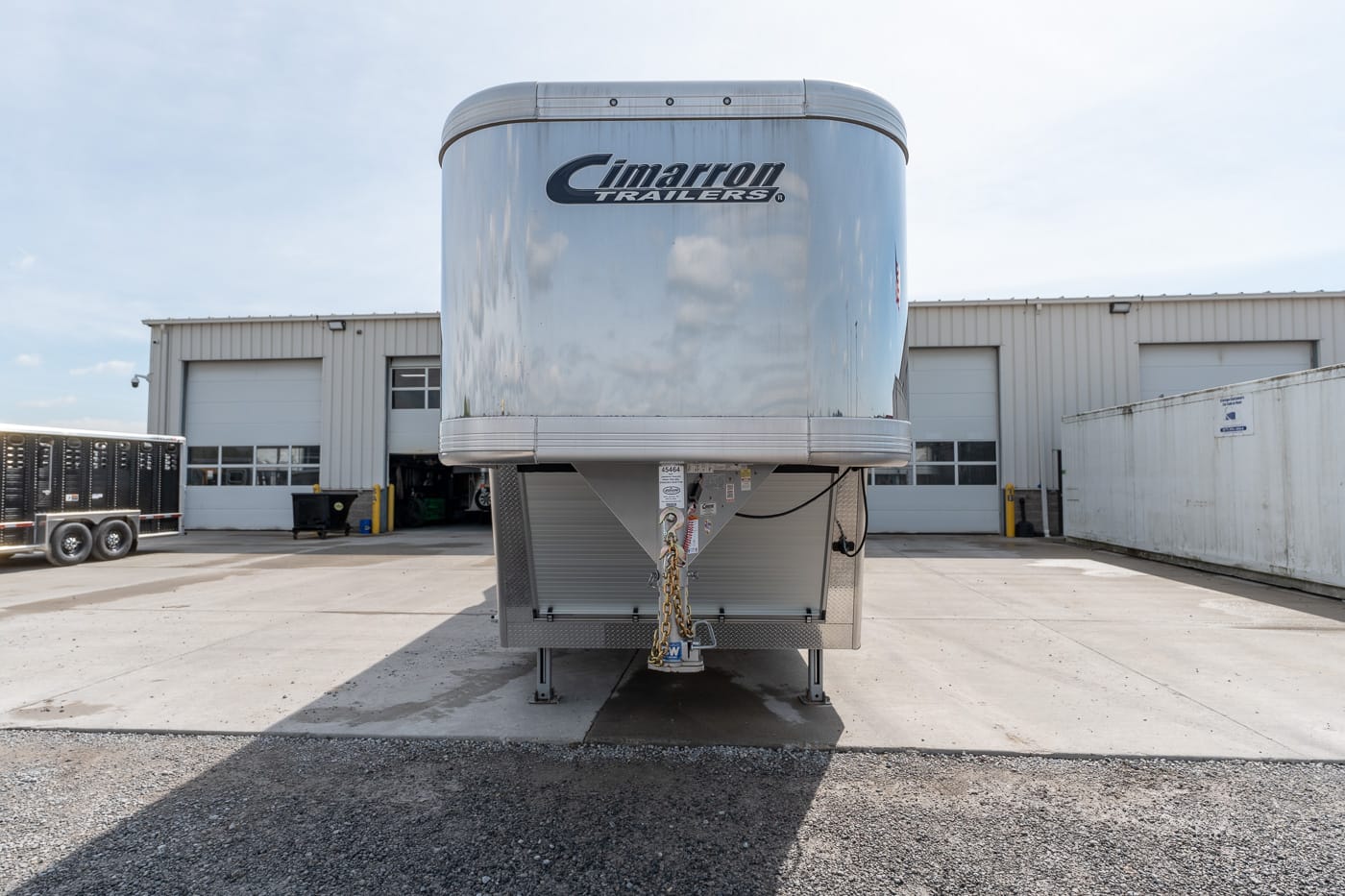 Front of a silver Cimarron trailer parked in an industrial lot with a loading bay in the background.