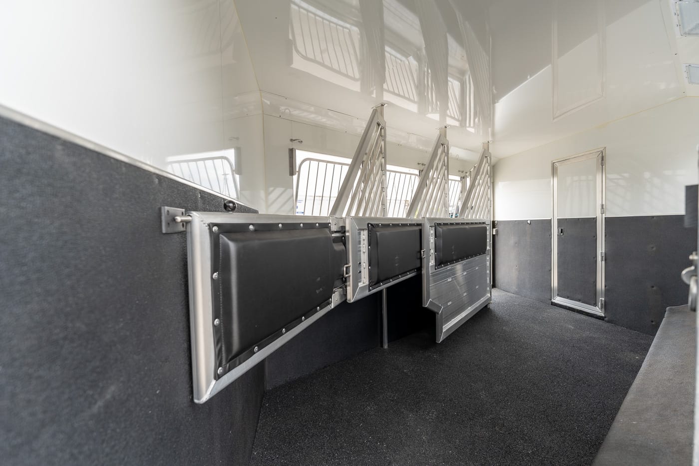 Interior of a horse trailer with row of padded stalls and metal dividers along the aisle의