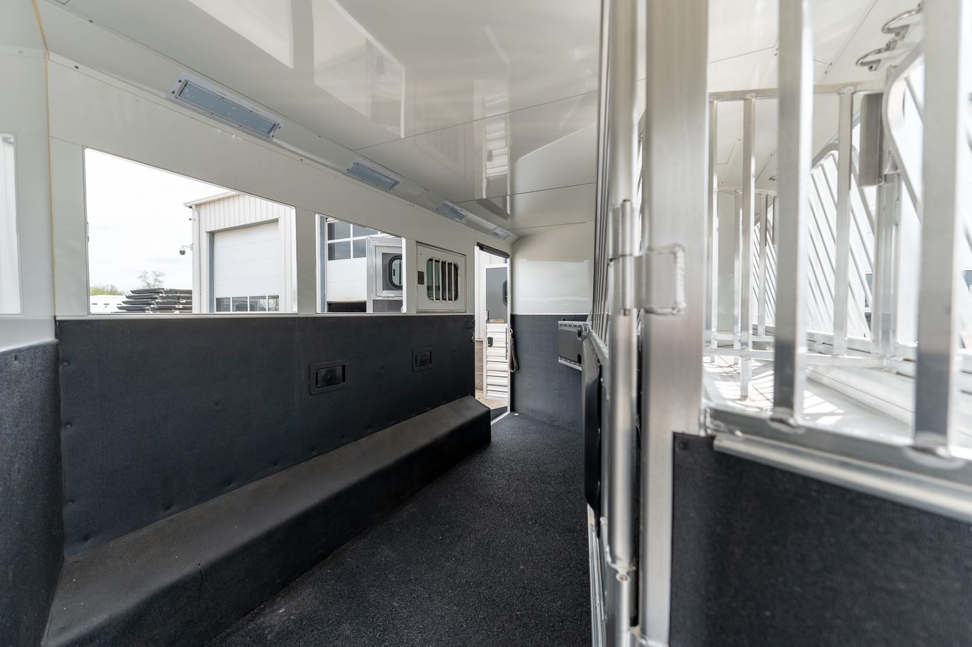 Interior of a white horse/trailer with a black rubber floor and metal stalls, viewed from the back toward the front with an open rear door