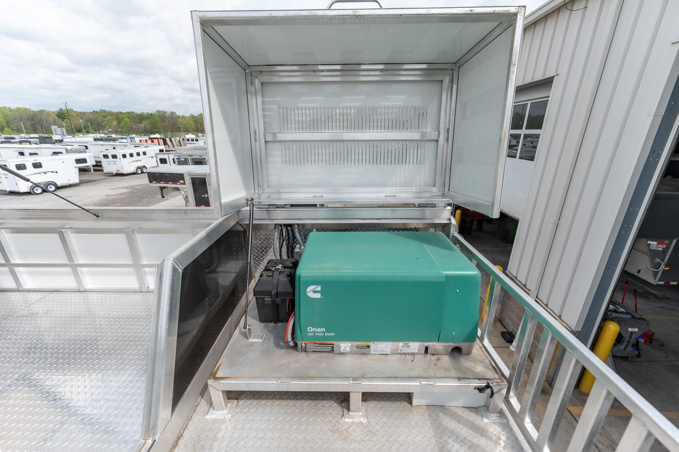 Green Onan generator installed in a metal utility truck bed with an open rear hatch and diamond-plate floor, outdoors in a lot of trailers.
