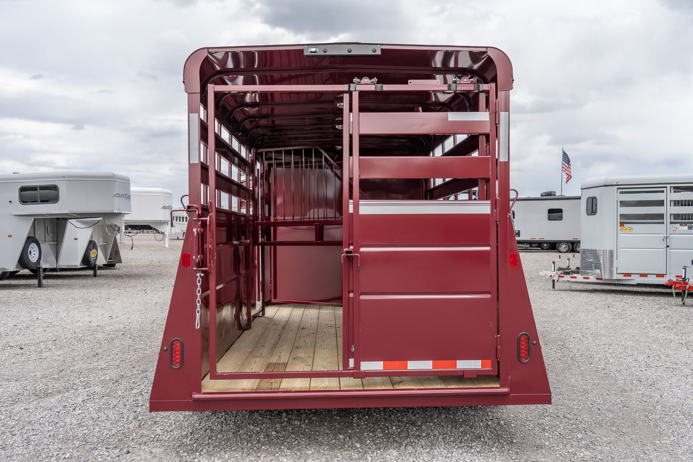 Open red livestock trailer interior with wooden floor and divider stalls, viewed from the rear (empty).