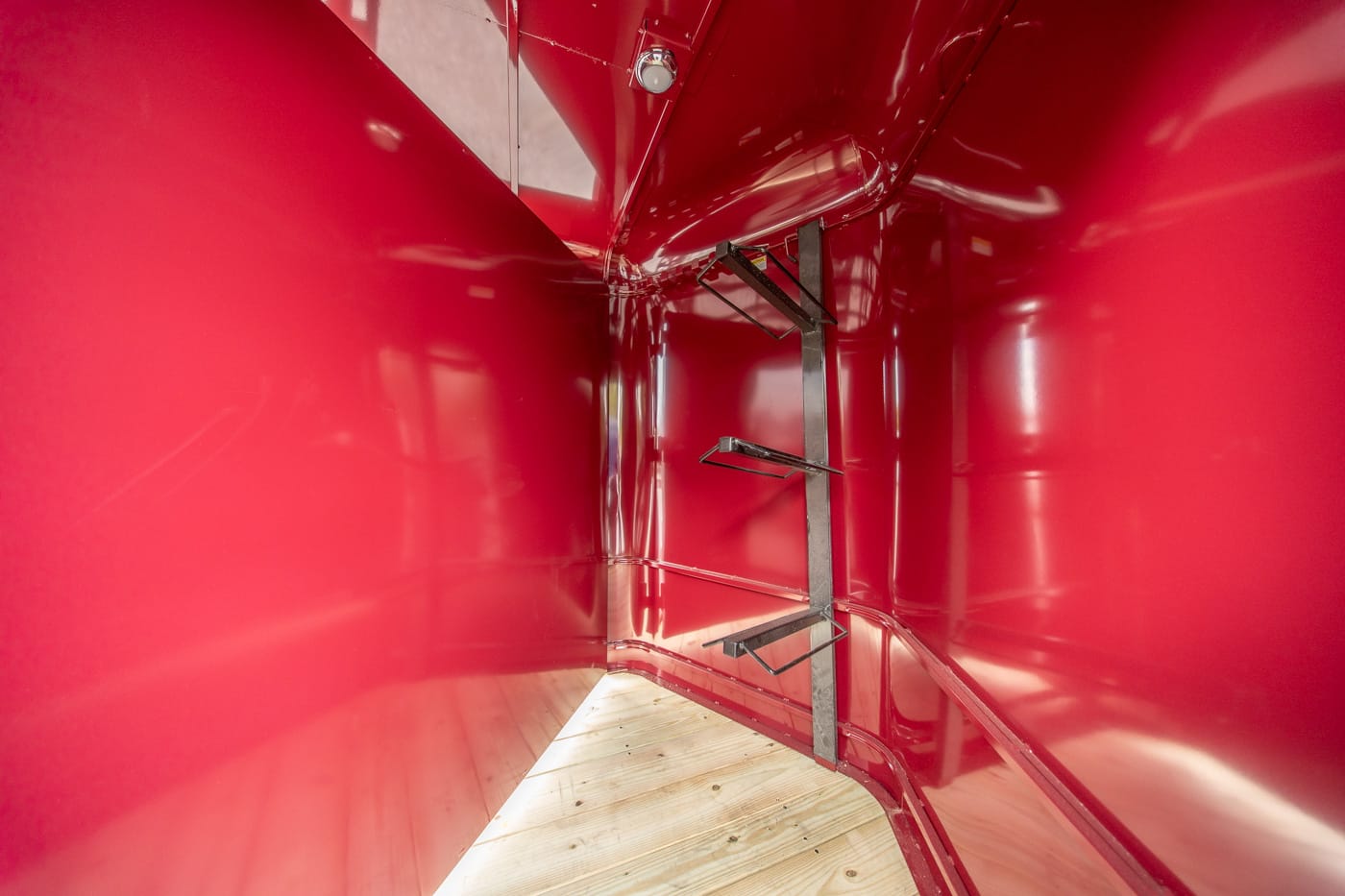 Interior of a red glossy trailer with a vertical steel support and fold-out metal brackets along the wall.