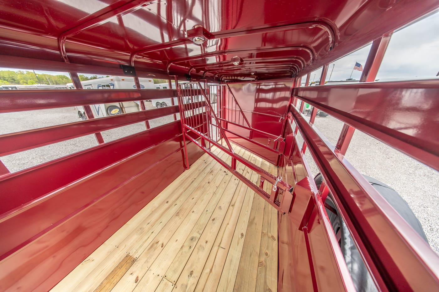 Interior of a red livestock trailer showing wooden floor, metal stalls, and side rails for animals, with a wheel visible outside.