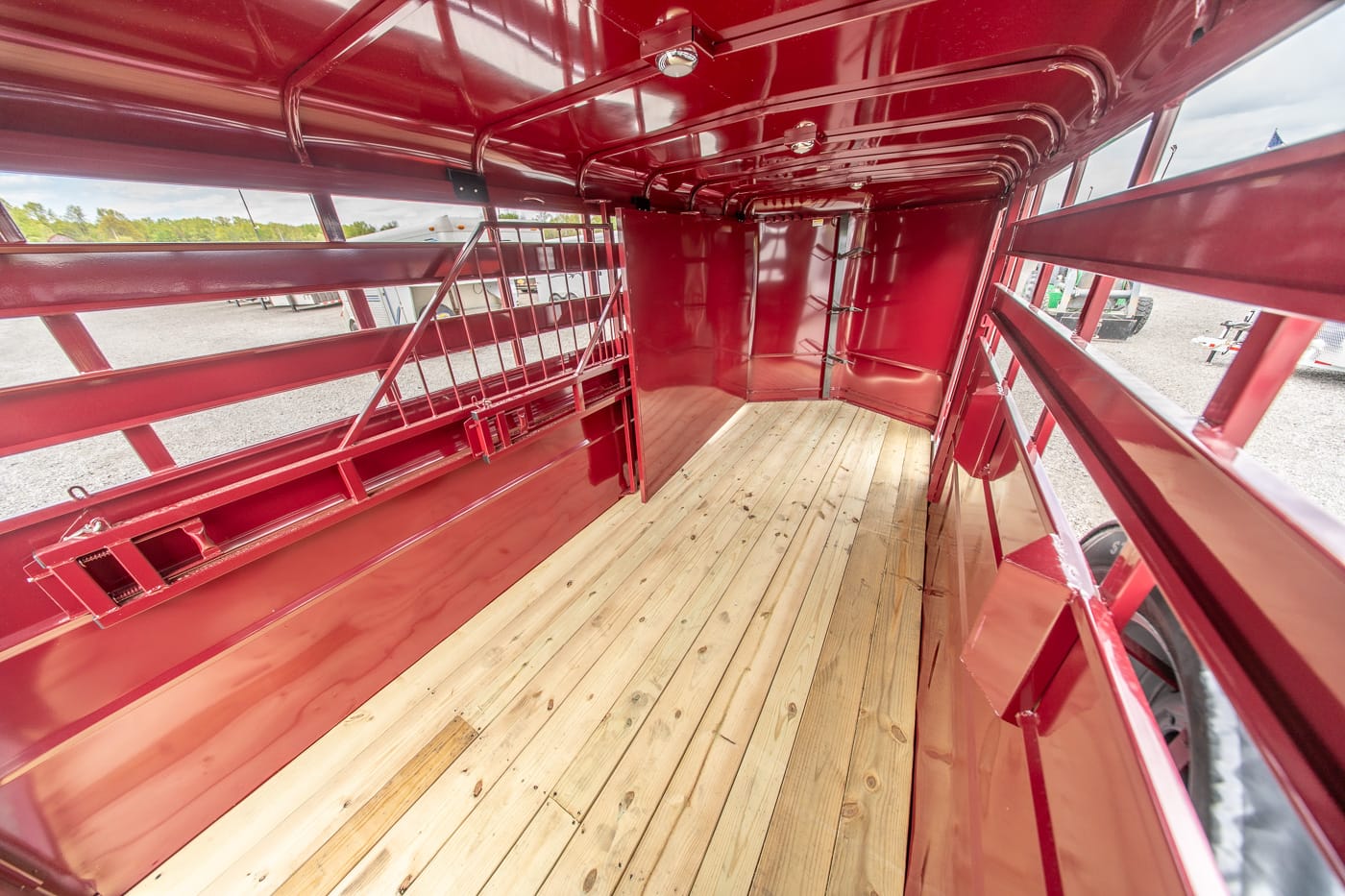Interior view of a red livestock trailer with a wooden floor and metal partitions, seen from the rear toward the front.