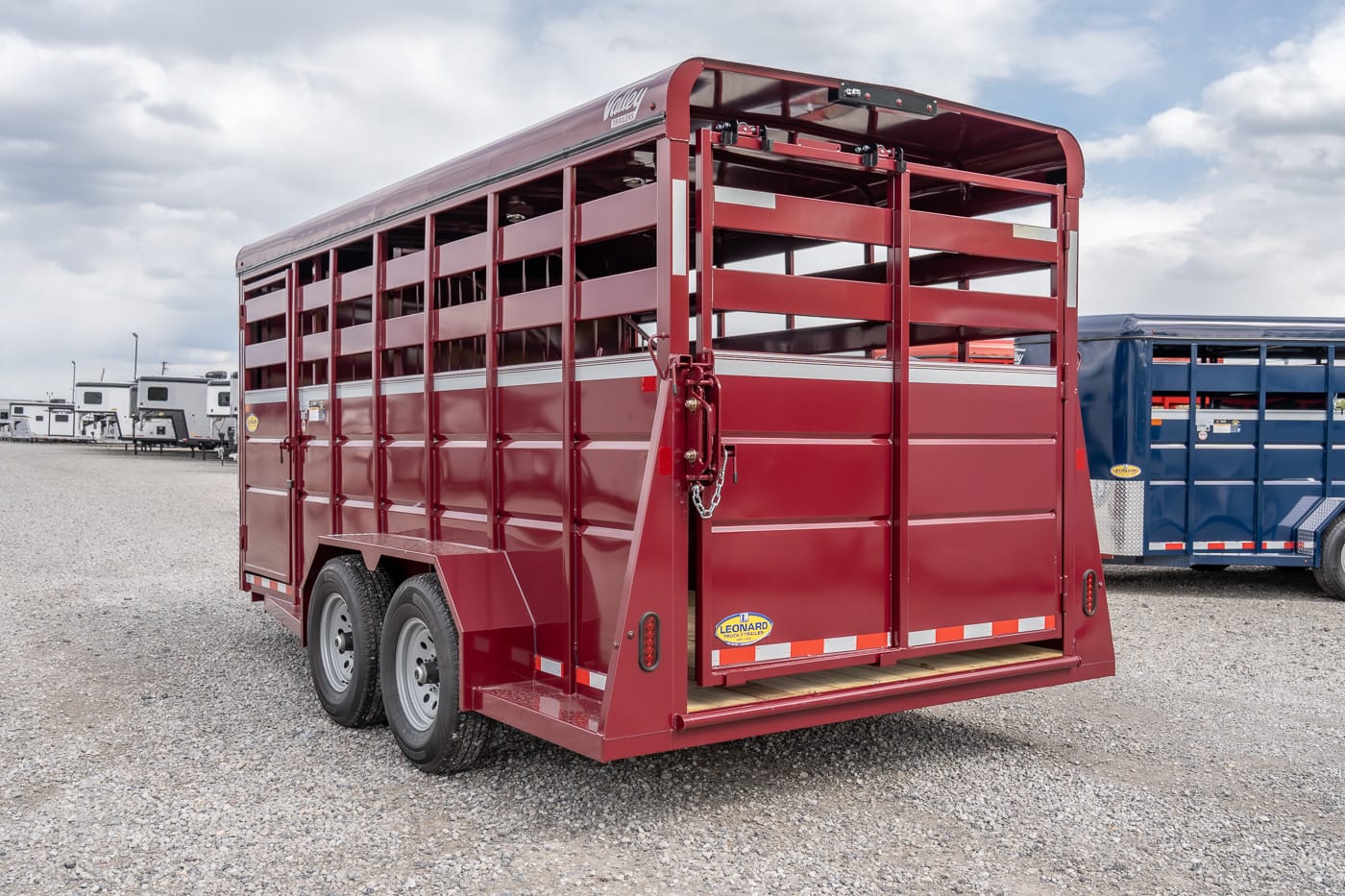 Red livestock trailer with ventilated slat sides and double-axle rear, parked on gravel.
