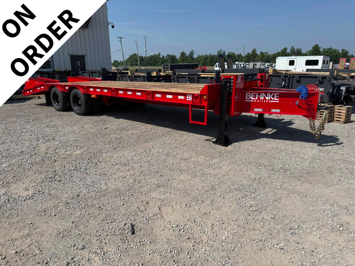 Red Behnke flatbed trailer on a gravel lot with a diagonal 'ON ORDER' banner in the top-left corner.