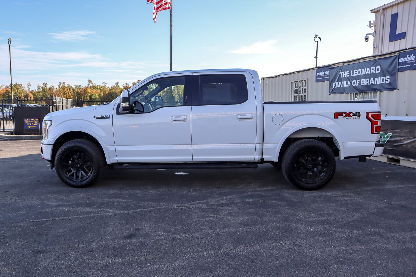 Side view of a white Ford F-150 pickup truck with black wheels in a dealership lot.