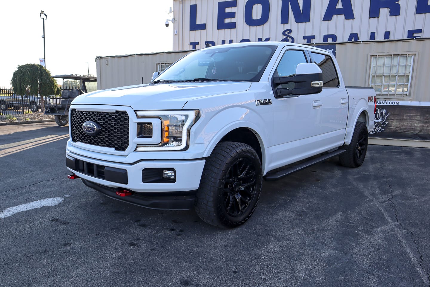 White Ford F-150 pickup with black wheels parked on a lot in front of a building with large blue lettering