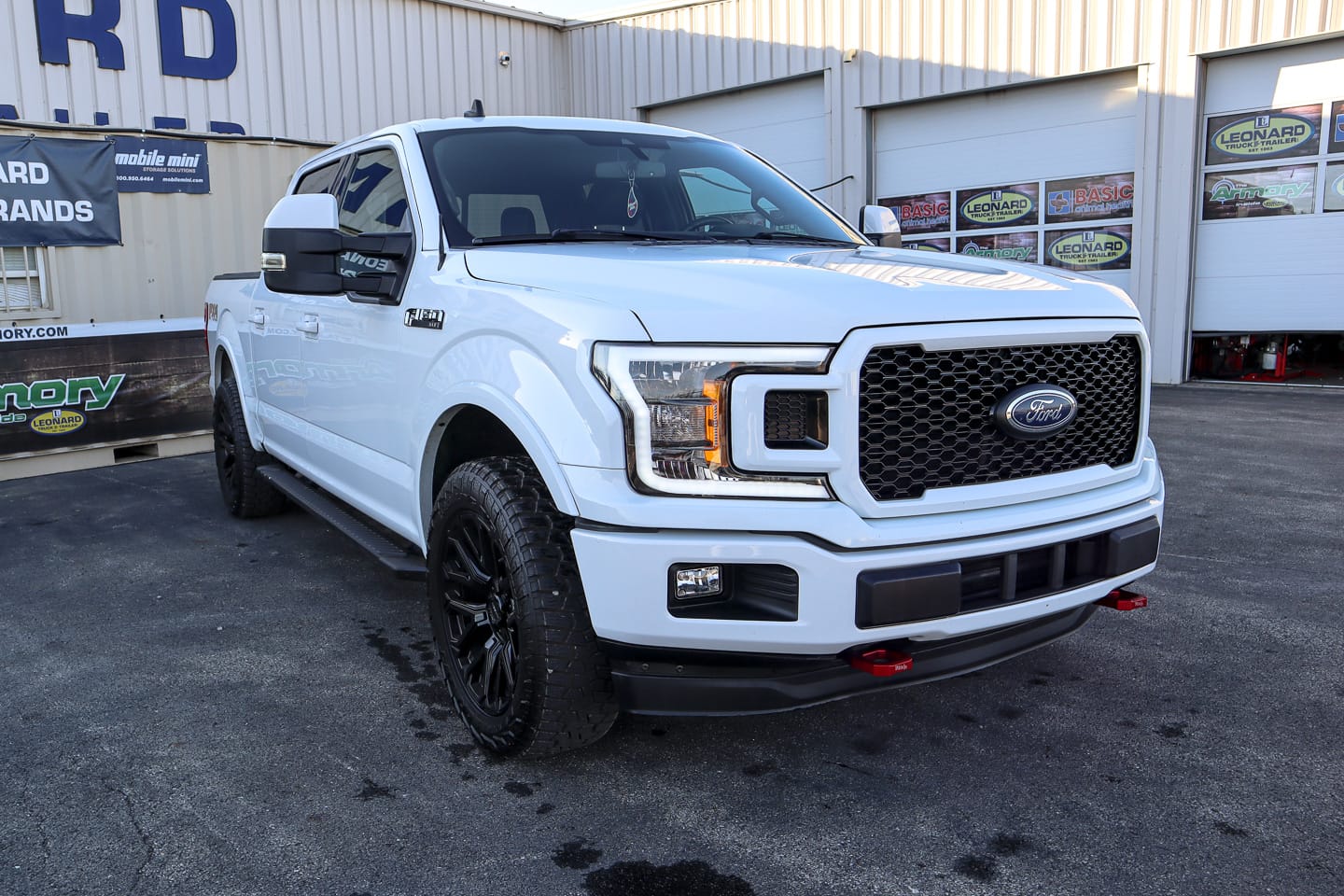 White Ford F-150 pickup at a dealership, front three-quarter view with a bold black grille and red tow hooks.