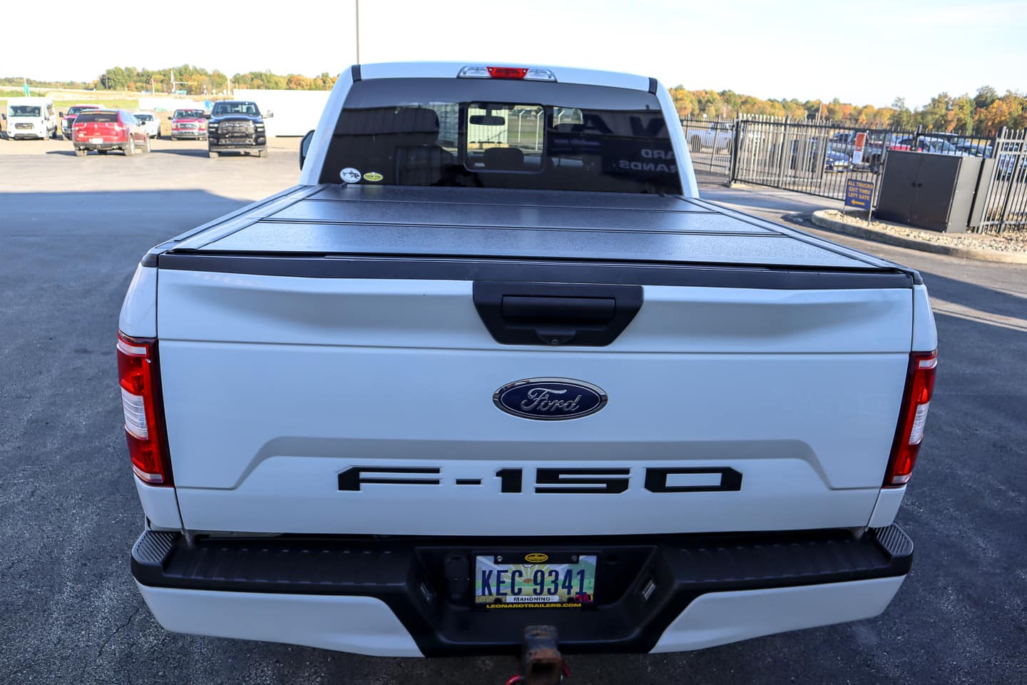 Rear view of a white Ford F-150 pickup with a black tonneau cover, license plate KEC 9341, and hitch in a parking lot setting