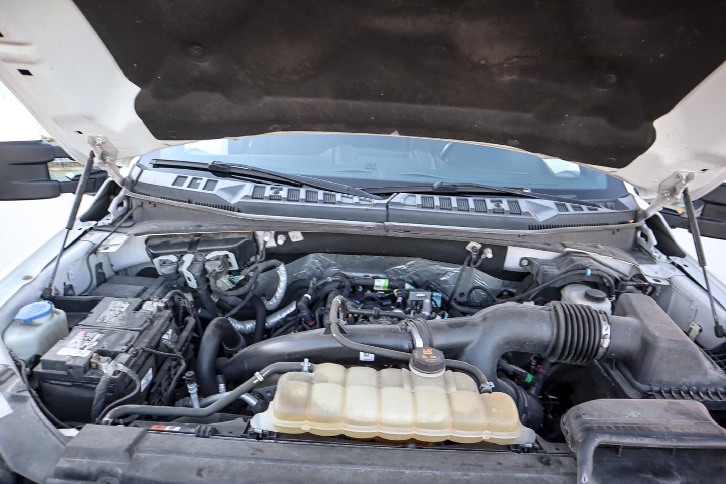 Open car hood showing the engine bay with battery on the left and a translucent coolant reservoir in the front center.