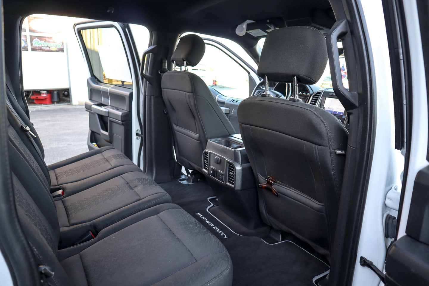 Interior of a black cloth-covered pickup truck with rear doors open, showing a spacious rear bench seat and center console area.