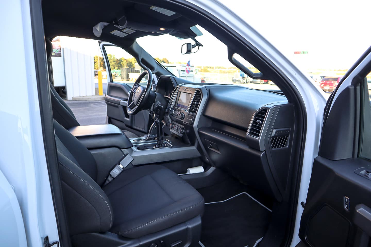 Interior of a white pickup truck shown from the open front passenger door, with the dashboard, steering wheel, and center console in view.