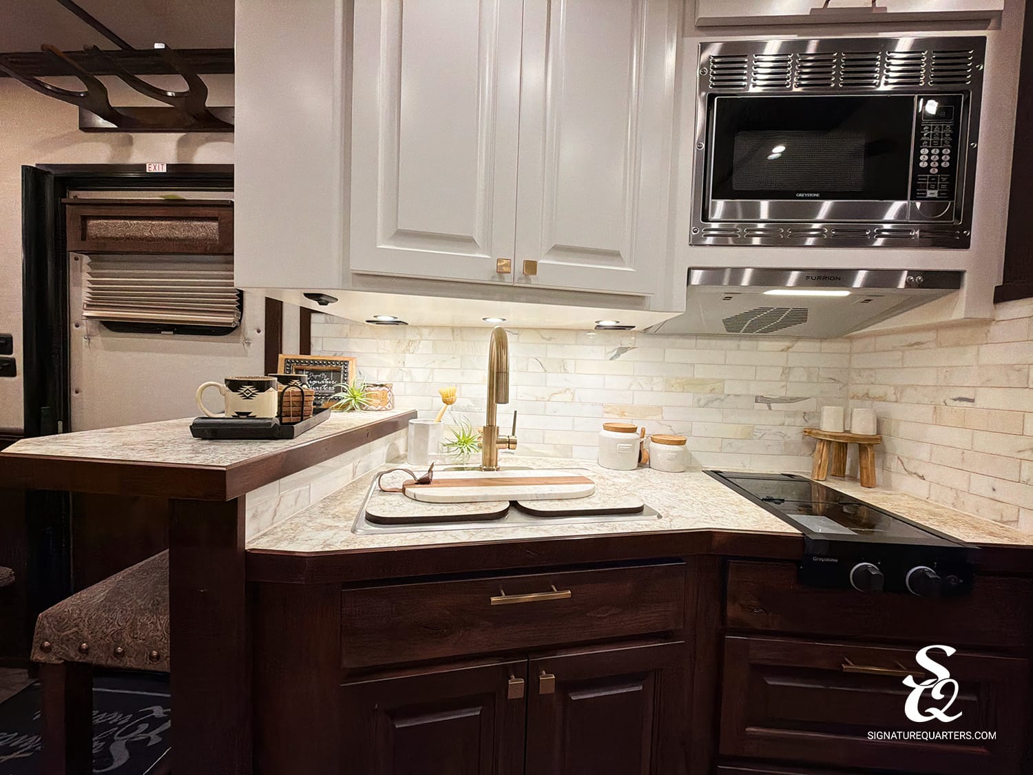 Compact kitchen with white upper cabinets, dark wood island, and stainless microwave over a tile backsplash.