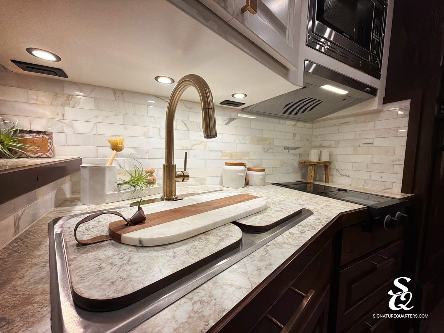 Modern kitchen sink area with a tall brass faucet, marble countertop, and a wooden marble-cutting board on the sink's drainboard.