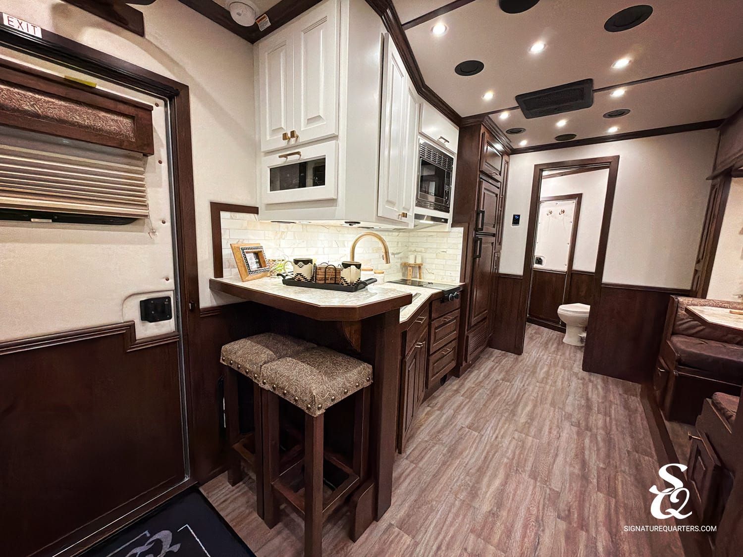 Luxurious RV kitchen with white cabinets, marble countertop, gold faucet, and dark wood island with stools.