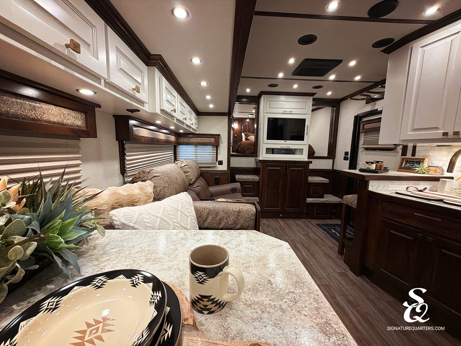 Luxurious RV interior: kitchen island, dining table with plates and a mug, and plush living area.